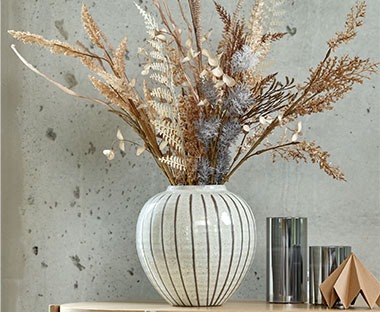 Бяла керамична ваза с изкуствени растения.