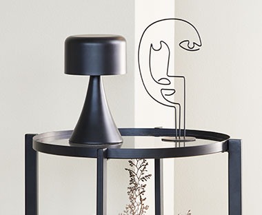 Лампа на батерии и скулптура въху малка маса за кафе.