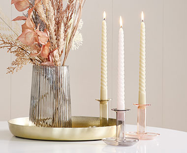 Ваза с изкуствено растени и свещи в свещници върху декоративен поднос.