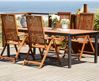 Дървена градинска маса с дървени градински столове на слънчев балкон.