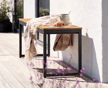 Дърване пейка с чаша и одеяло на слънчев балкон.