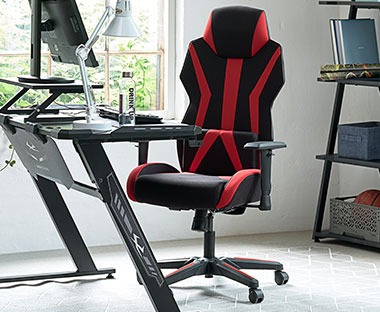 Ергономичен геймърски стол с елементи в червено и геймърско бюро.