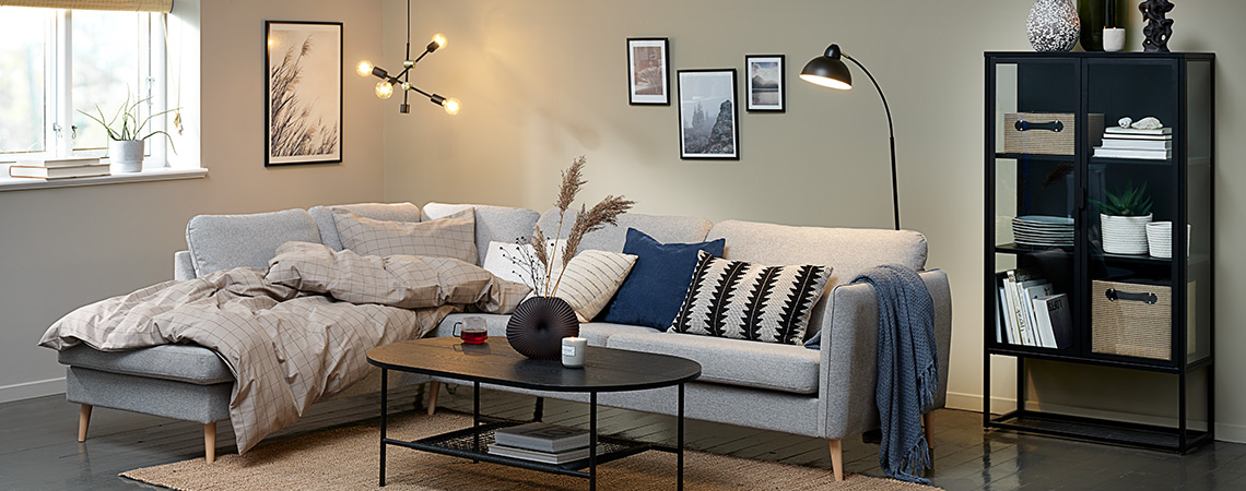 Комфорт в дневната с голямо ъглово канапе, завивка, декоративни възглавници и приятно осветление.