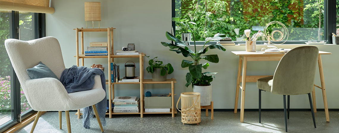 Сиво кресло до прозореца, бамбуков разделител за стая. Бамбуков фенер на пода до бамбуково бюро и маслинено зелен кухненски стол.
