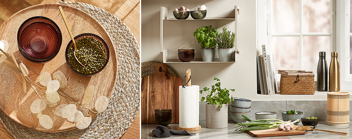 Стъклени чаши върху плетена подложка и керамични чаши с пресни билки на стенен рафт в кухня
