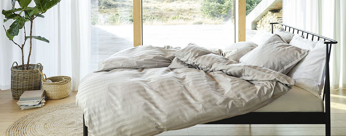 Спалня с черно метално легло, завивки и възглавници, покрити с раирано спално бельо в светлосиво и бяло