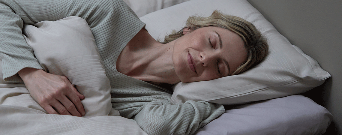 Жена, спяща настрани в легло с бяла възглавница и завивка.