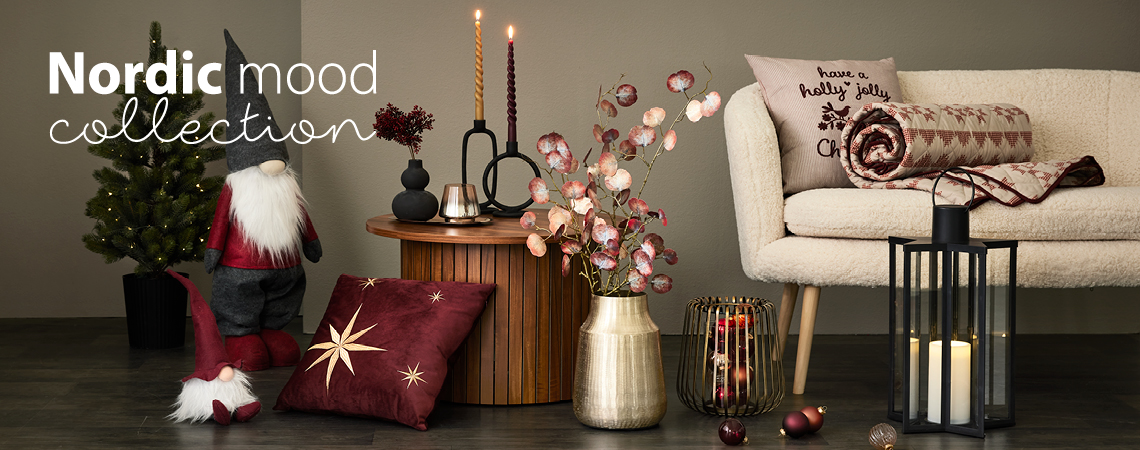 Коледни елфи, възглавници, златна ваза с изкуствено цвете, златен свещник и черен фенер пред бял диван.