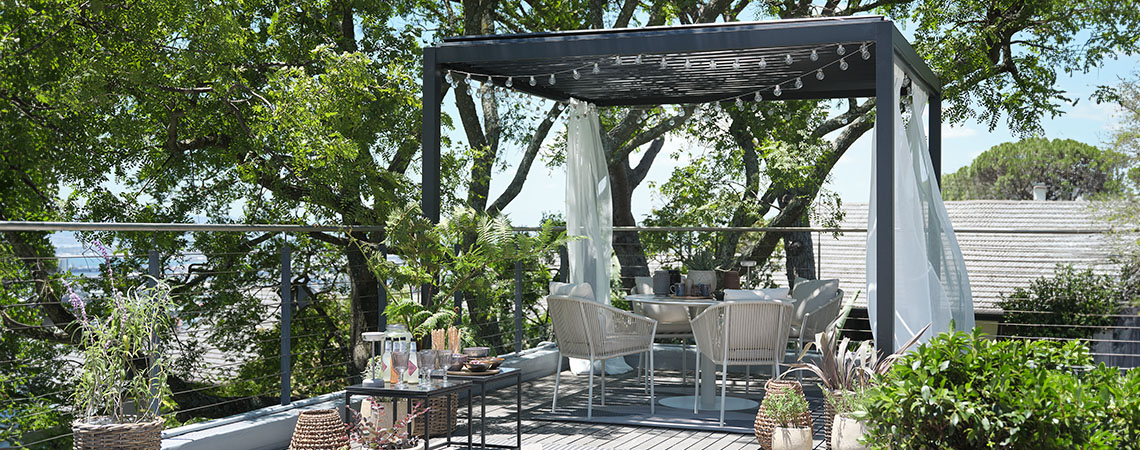 Метална пергола с покрив, декорирана с воалирани завеси и лампички във вътрешния двор