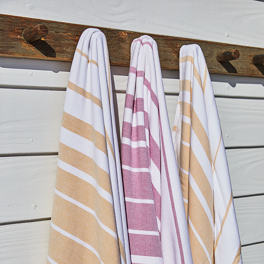 Плажни кърпи на райета в бяло, оранжево и розово, окачени на дървена стена.