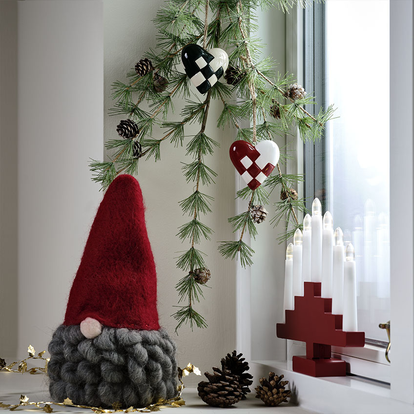 Коледен елф с червена шапка и сива брада и червена арка от свещи.