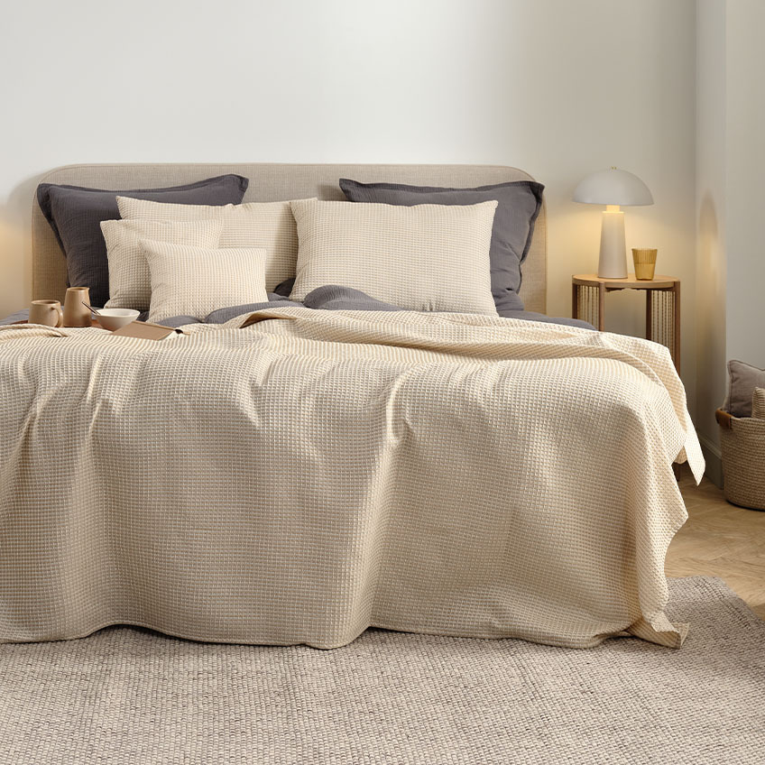 Кувертюра, възглавници за гръб и калъфка за възглавница в топъл бежов цвят на легло в спалнята.