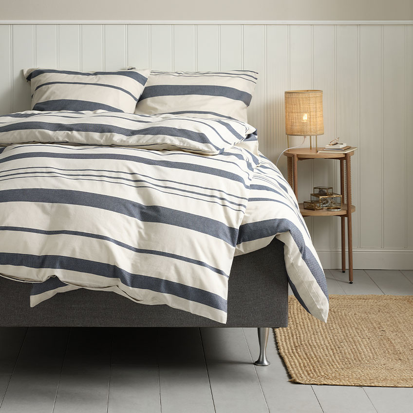 Комплект памучно спално бельо в бяло със сини ивици на леглото в спалнята.