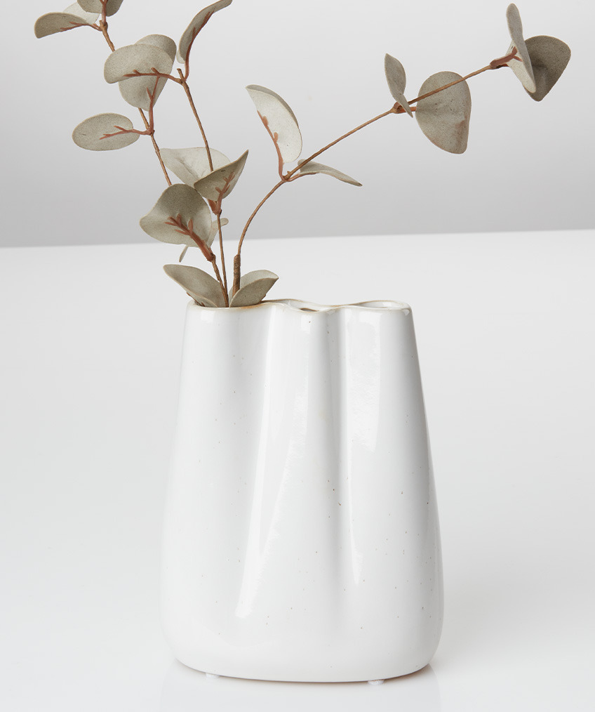 Бяла ваза с органични линии и вълнообразни ръбове и изкуствена клонка.