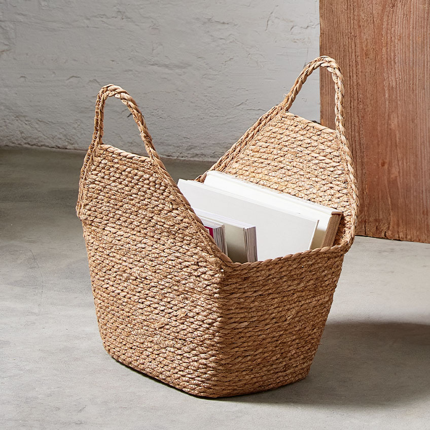 Плетена кошница с дръжки, изработена от папур, с книги и списания вътре.