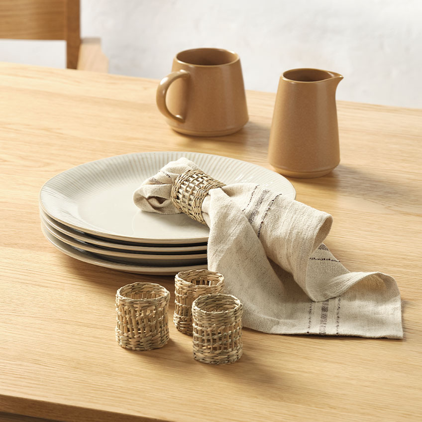 Каничка за мляко, чаша, платнена салфетка и пръстени за салфетки на масата за хранене.