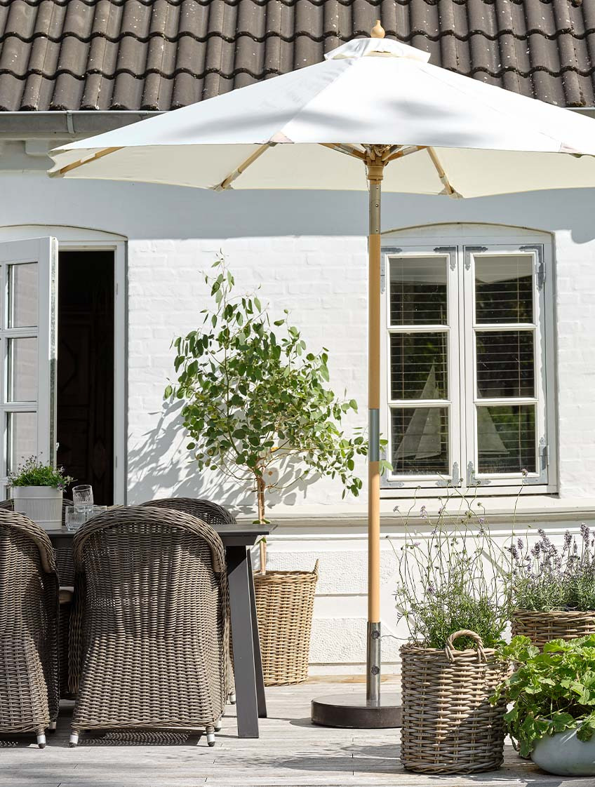 Класически бял градински чадър на двора с градинска маса и градински столове.