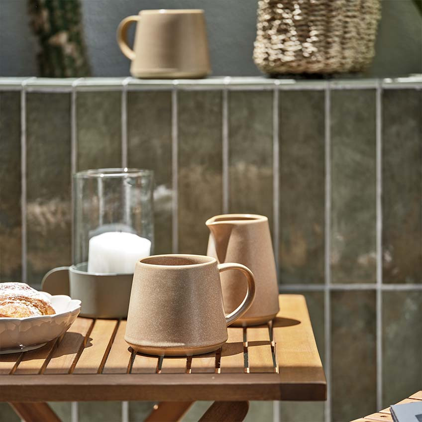 Чаша за кафе и каничка за мляко на малка дървена градинска маса.