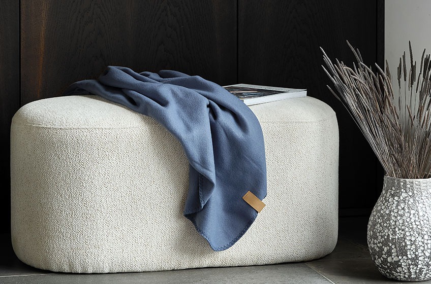 Белезникава табуретка със синьо одеяло отгоре, до сиво-бяла ваза