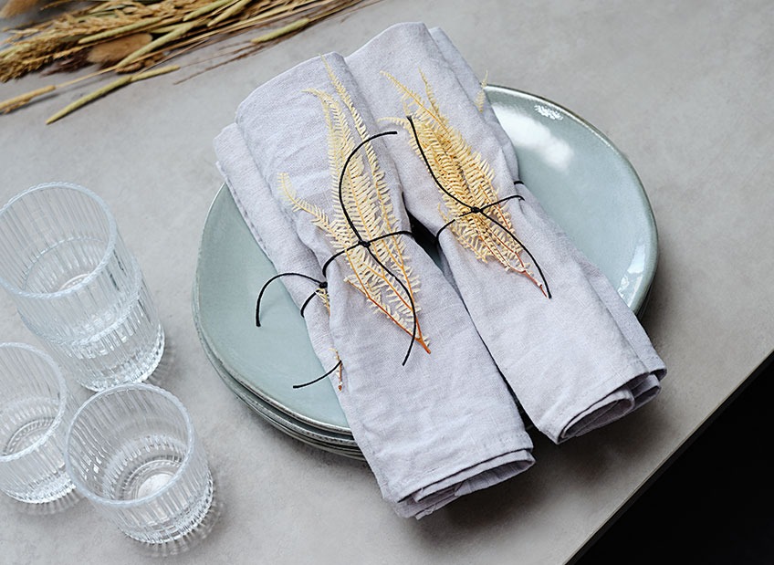 Подредена маса с чинии, чаши и текстилни салфетки, украсени със сухи листа.