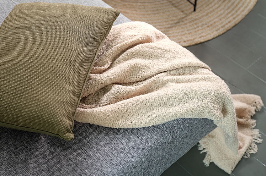 Зелена възглавница и плетено одеяло върху сив диван