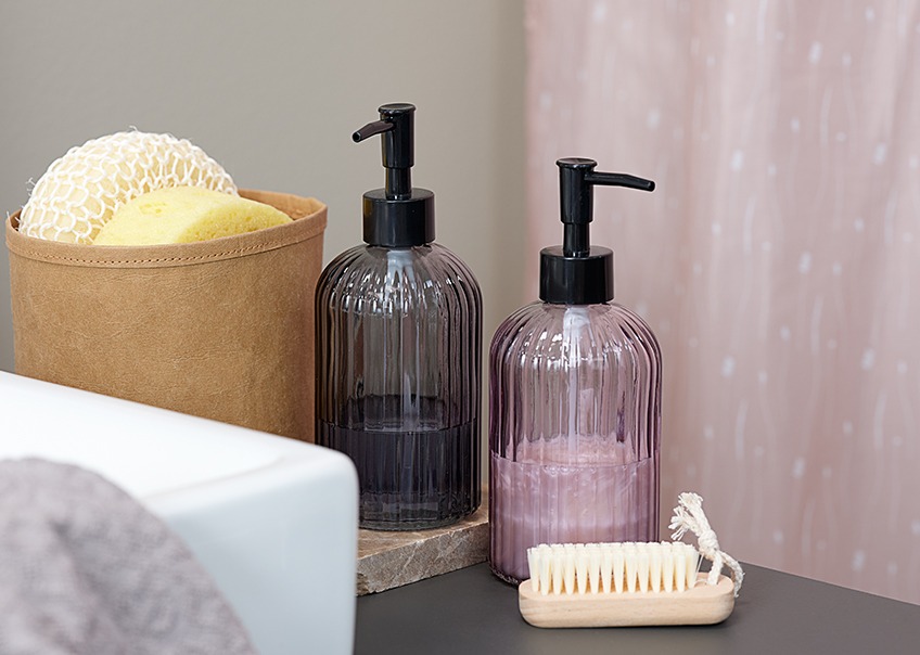 Стъклен диспенсър за сапун в различни цветове, гъби за баня и четка за нокти.