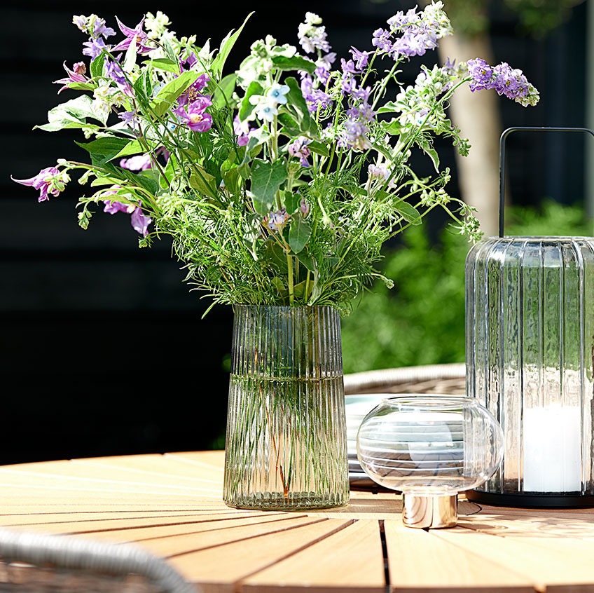 Стъклена ваза и фенер на градинска маса.