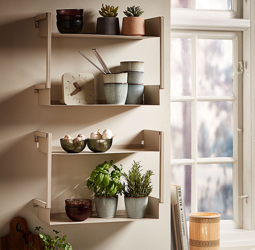 Стъклени купи, керамични чаши и пресни билки на стенен рафт в кухня