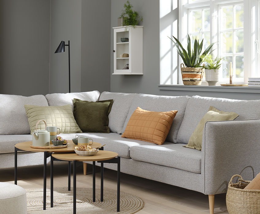 Обстановка в дневната със сив диван и оранжеви, зелени и бежови възглавници