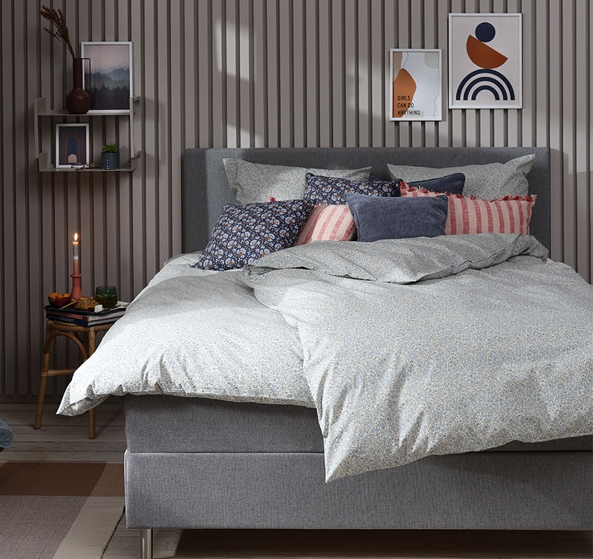 Спалня със синьо флорално спално бельо и декоративни възглавници в сини и розови цветове