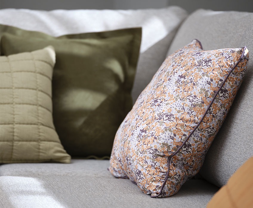 Сив диван с възглавници с флорални и зелени мотиви