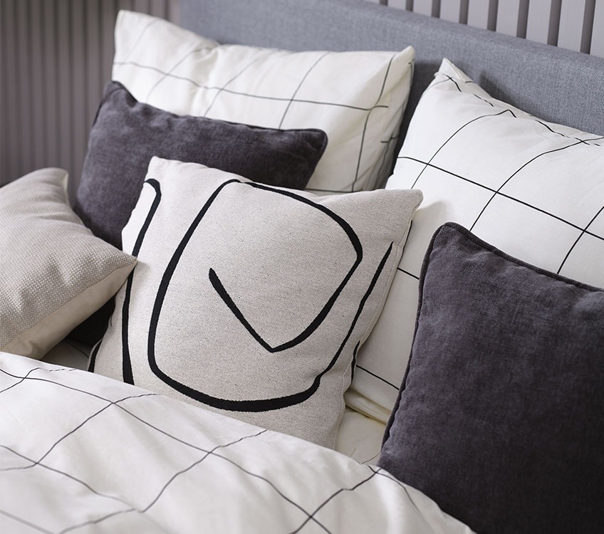 Спалня с бяло и черно спално бельо и сиви декоративни възглавници
