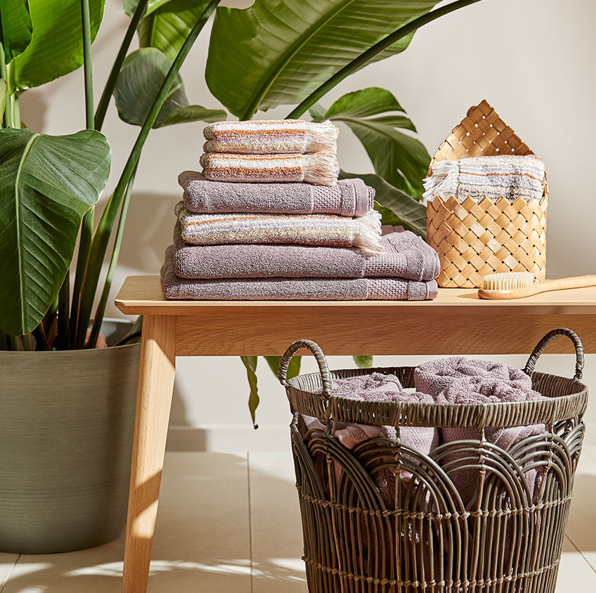 Памучни кърпи и плетена кошница върху пейка в банята