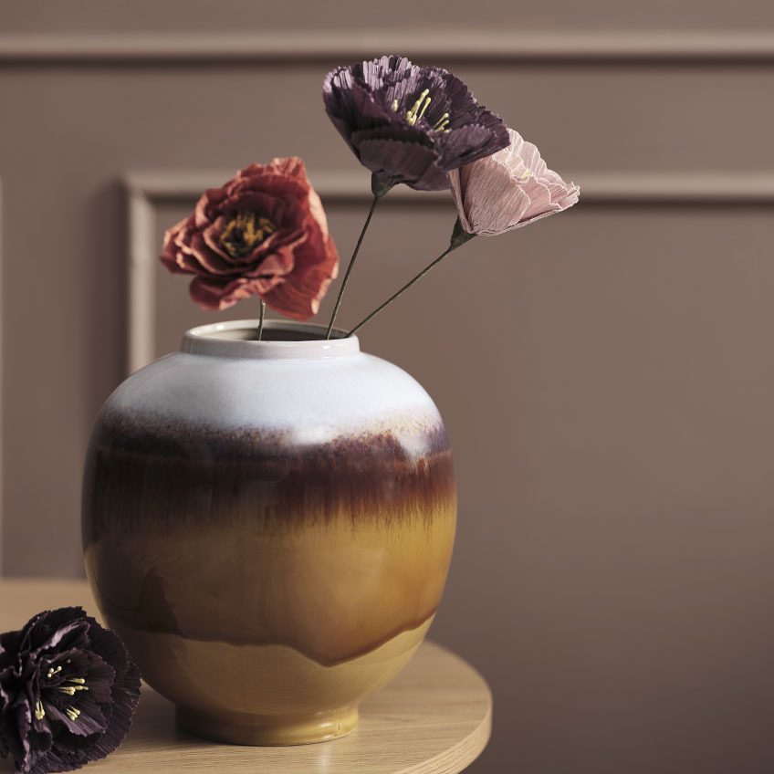 Многоцветна ваза на маса с изкуствени цветя в червено, лилаво и розово.