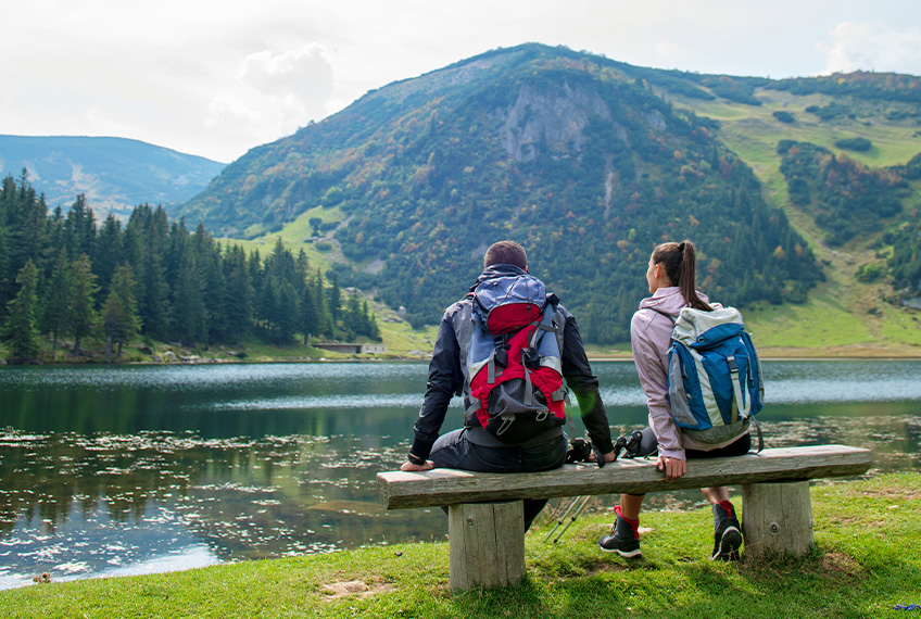 Мъж и жена седят на пейка с изглед към планинското езеро