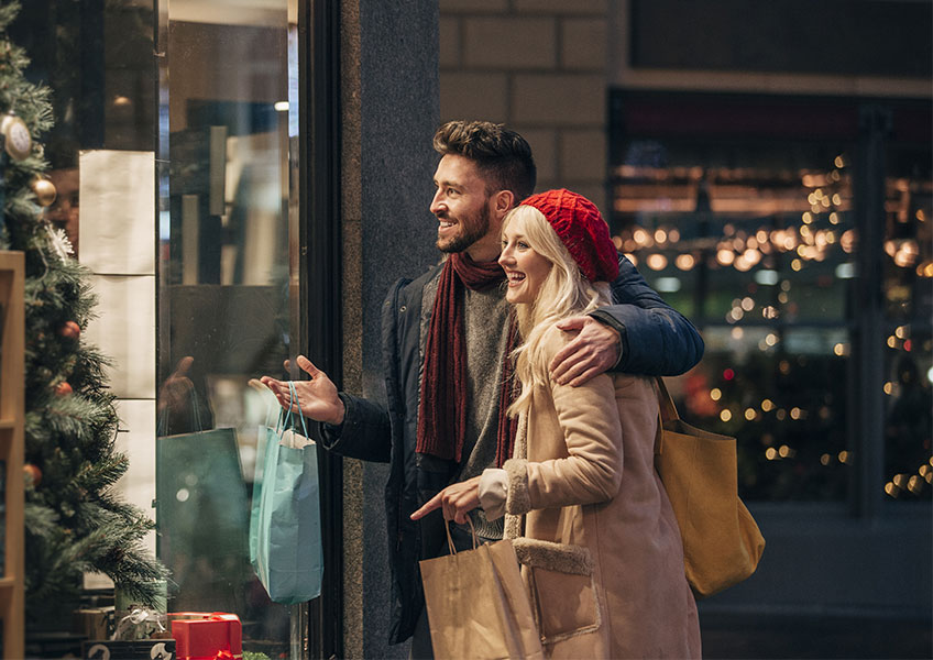 Млада двойка пазарува за Коледа и гледа витрина на магазин
